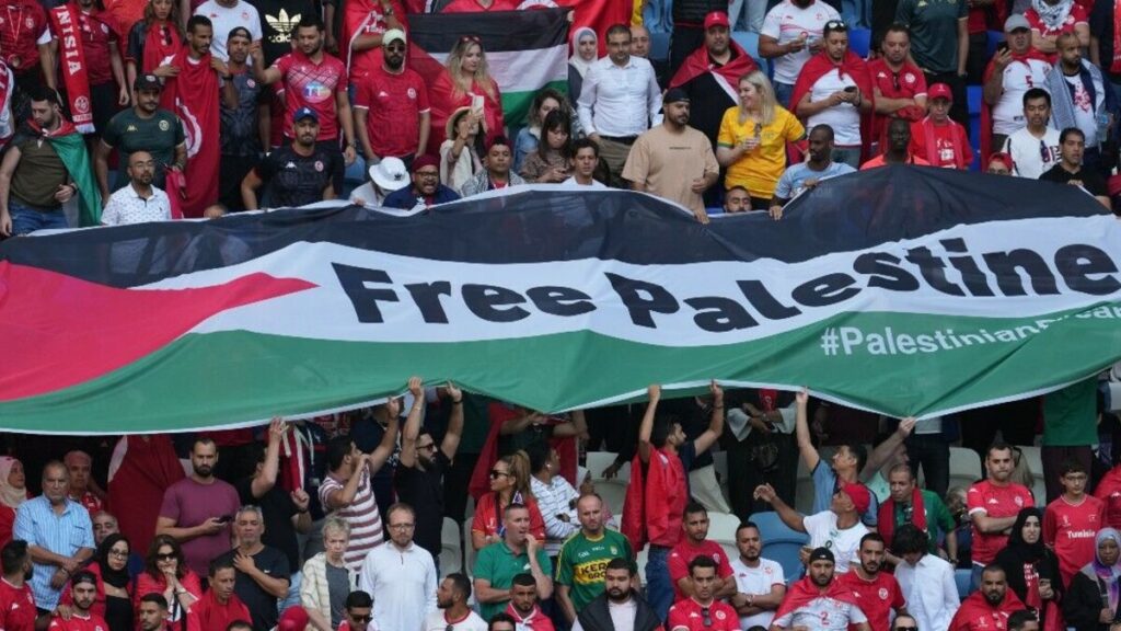 Illustration d'une action de boycott sportif possible. une foule de supporters dans un stade avec une banderole : drapeau palestinien et Free Palestine