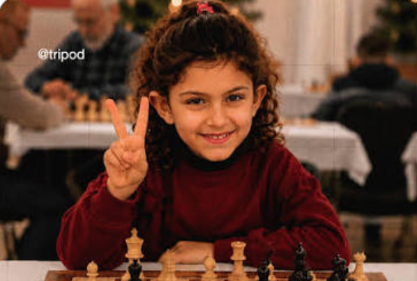 Loryn Abdul Samad à une table d'échecs qui sourit et fait un signe V avec sa main droite
